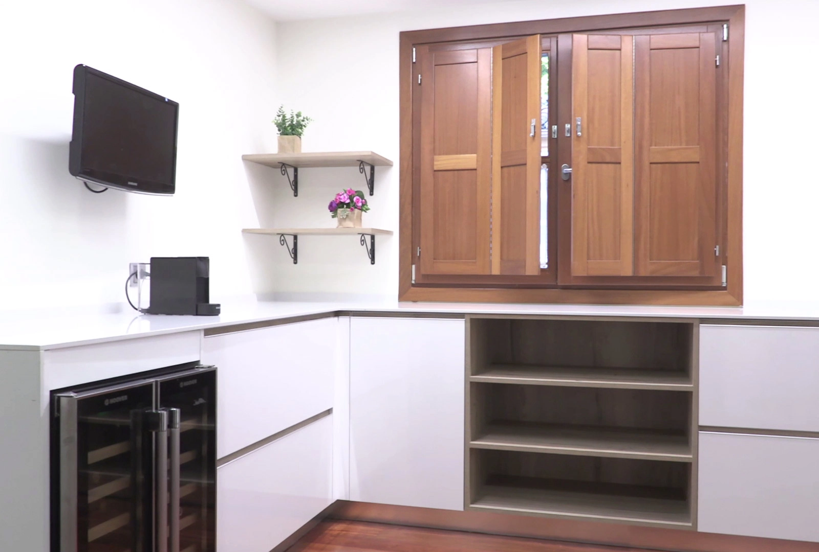 Zona de office contigua a la cocina con muebles en forma de ele en color blanco con detalles en madera, con vinoteca, TV y estantes