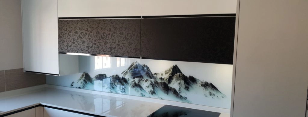Vista frontal y en detalle de cocina en laminado blanco brillo con detalles en estampado negro y pared sobre encimera con imagen de montañas