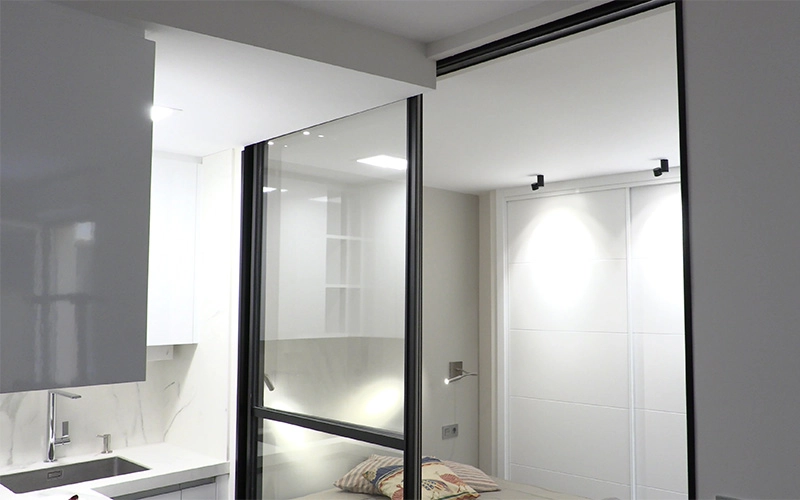 Puerta corredera en cristal con marco negro brillo para separar cocina y dormitorio en estudio pequeño en León