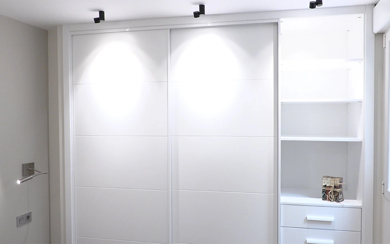 Vista de armario iluminado fabricado en lacado blanco con dos puertas correderas, baldas y cajones en el lateral - Proyecto Reforma de estudio pequeño en León