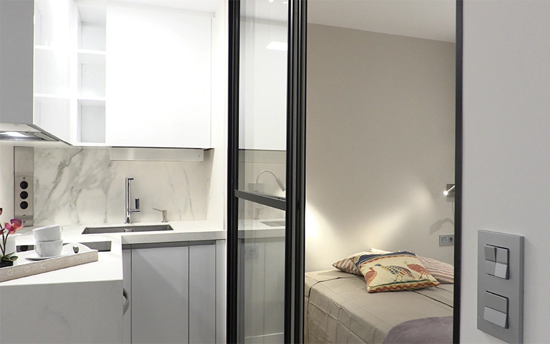 Cocina y dormitorio separados por puerta corredera en cristal y carpintería negro brillo - Proyecto Reforma de estudio pequeño