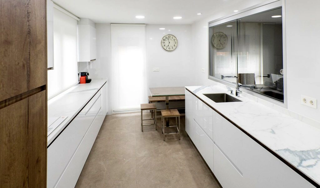 Vista frontal de cocina moderna con carácter nórdico y frentes en paralelo, encimeras blancas y gran espacio de almacenaje.