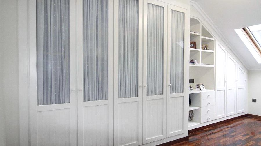 Vista lateral de armario alto blanco con puertas con cristal y tiradores en forma de bola para habitación abuhardillada