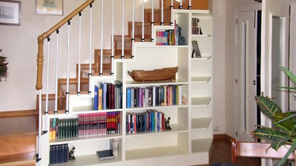 Vista del hueco de la escalera funcional con estanterías en color blanco llenas de libros y objetos decorativos para aprovechar espacio.