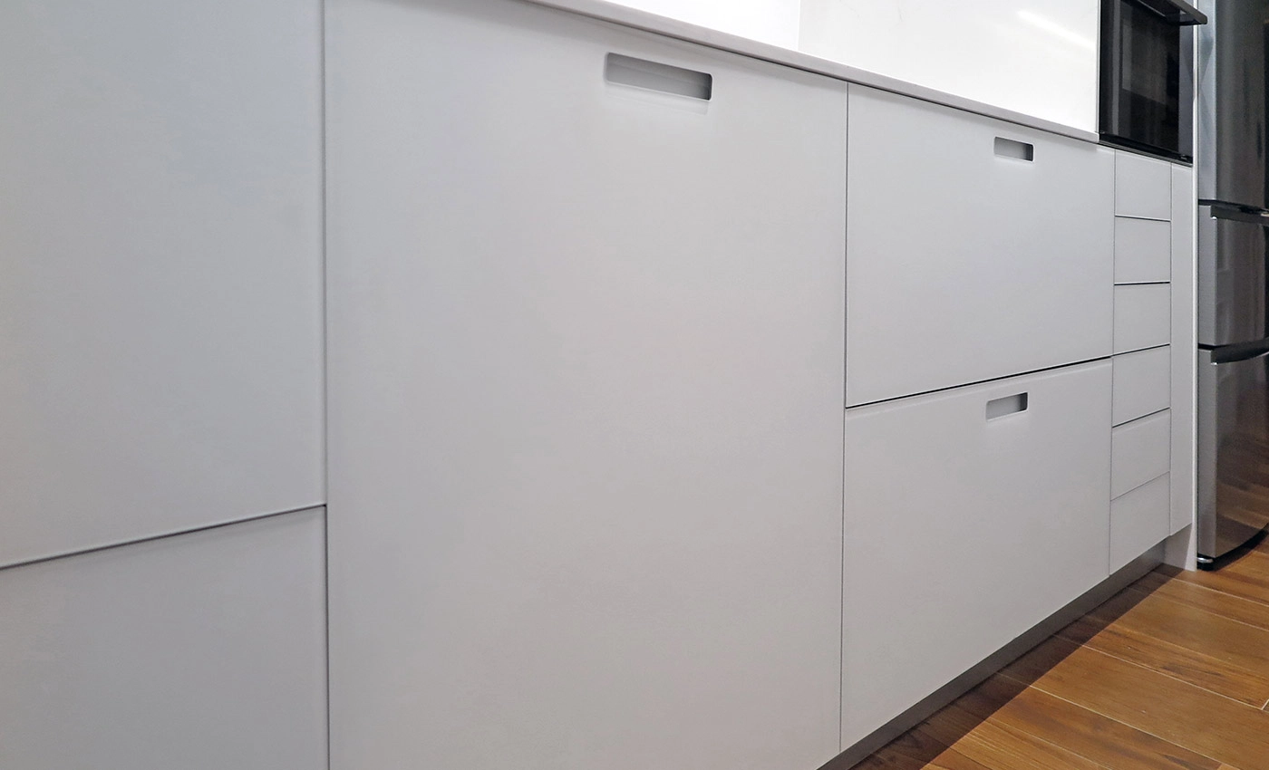 Vista lateral en detalle del mobiliario bajo de cocina blanca con gran capacidad de almacenamiento y electrodomésticos al fondo