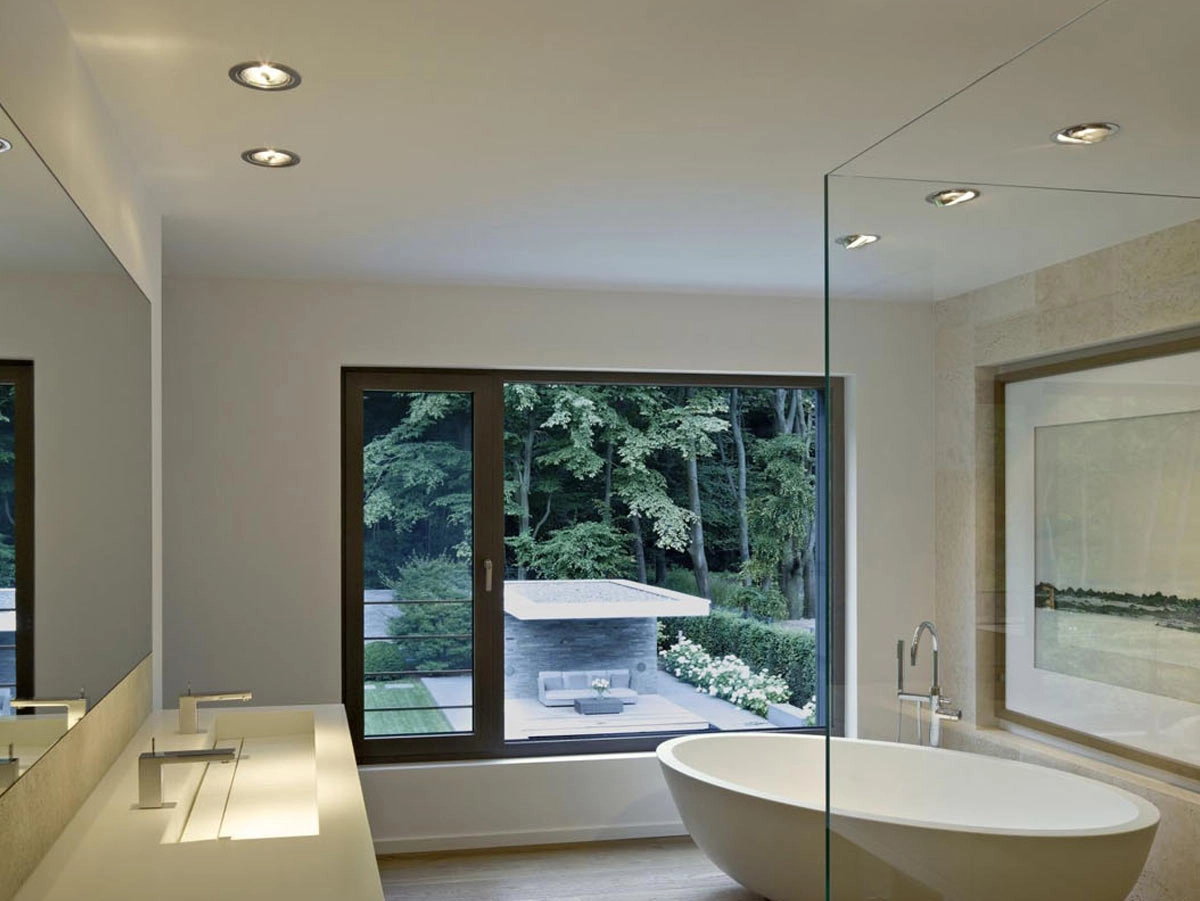 Vista frontal de baño con equilibrio de luces a través de focos situados en línea en el techo con bañera blanca y lavabo