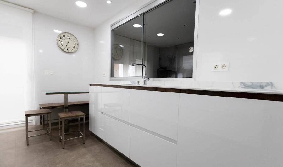 Frente de muebles bajos de cocina moderna en color blanco brillo con diseño de puerta con tirador incorporado y mesa amplia al fondo