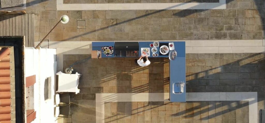 Vista cenital de composición de cocina para exterior en acero situada en una terraza con cocinero trabajando en ella