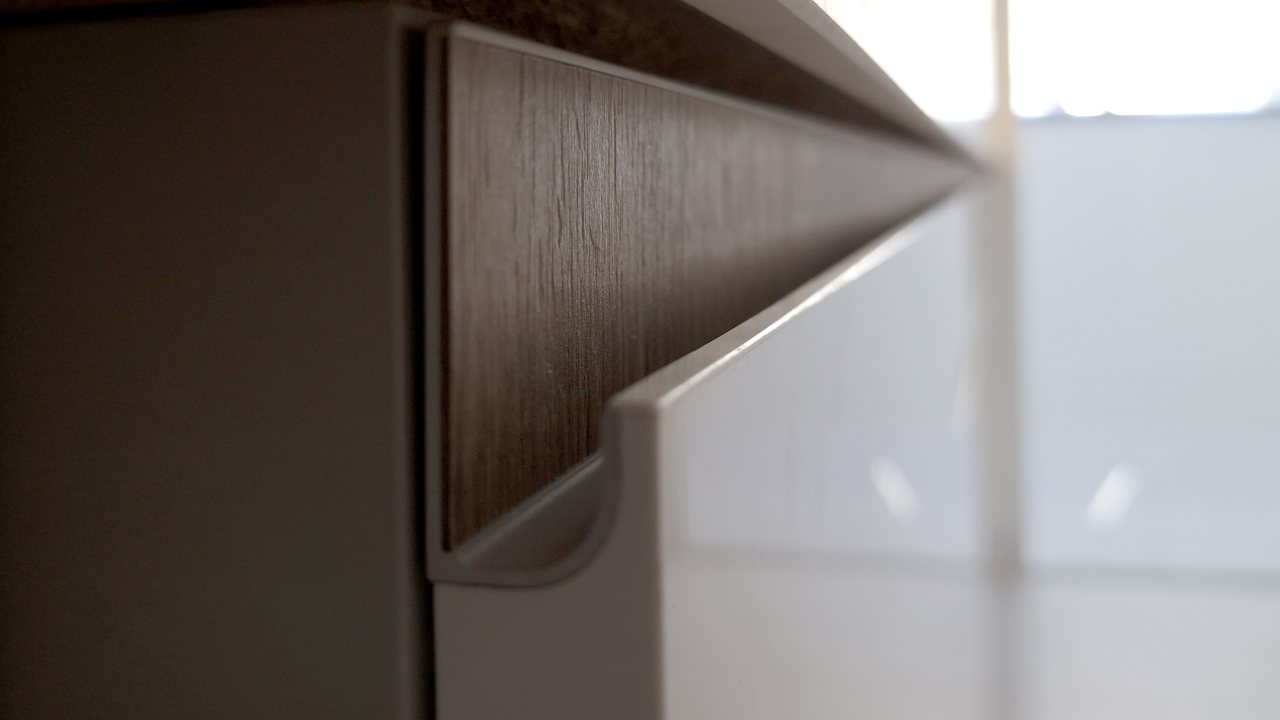 Detalle de tirador de puerta de cocina modelo Fussion de Senssia color blanco brillo con camisa en acabado madera