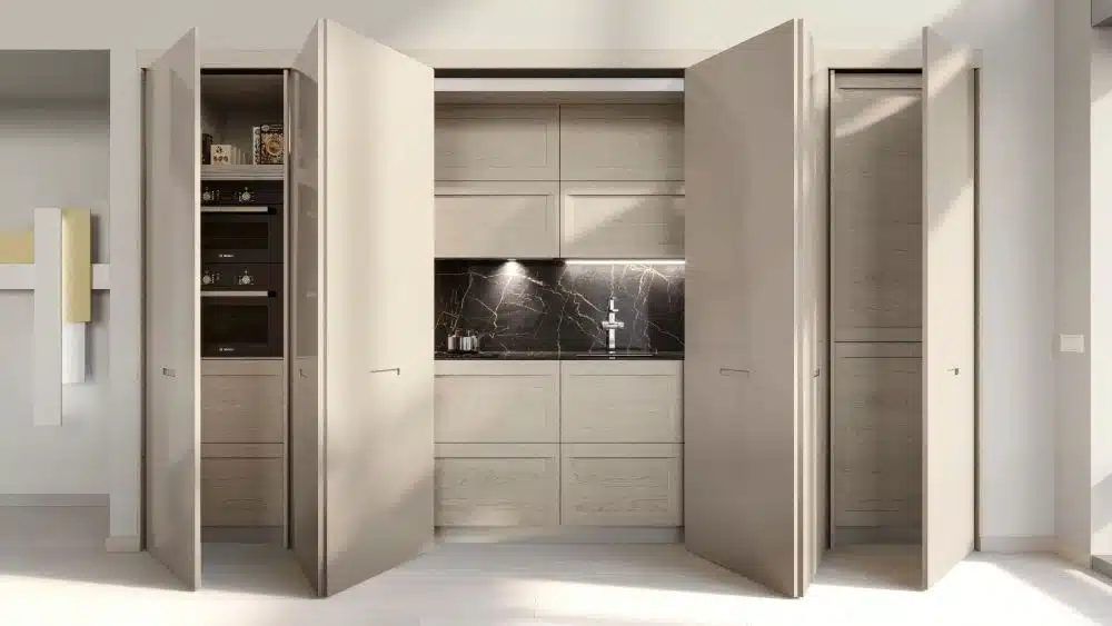 Vista frontal de armario de cocina amplio y blanco con puertas escamoteables abiertas que muestran la cocina