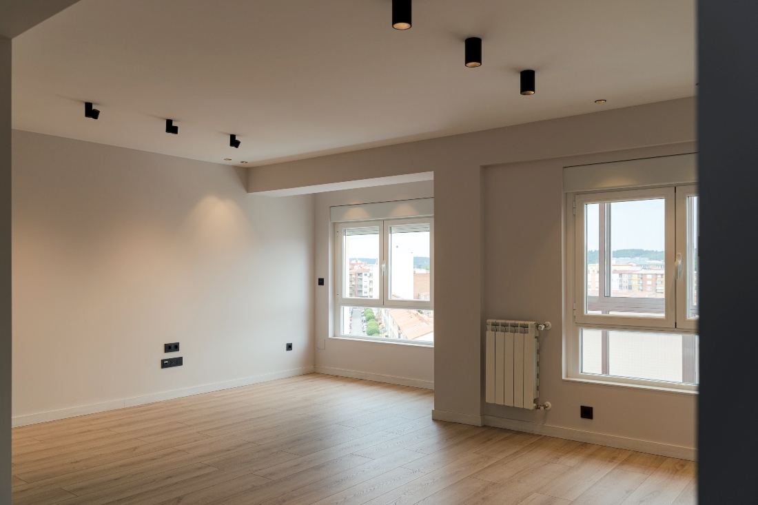 Habitación blanca y vacía de vivienda con dos ventanas grandes que generan luz en la sala