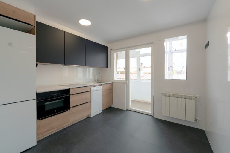 Visita de lateral de cocina amplia y luminosa con puerta de cristal con salida a patio interior, con mobiliario en negro y en madera con electrodomésticos integrados