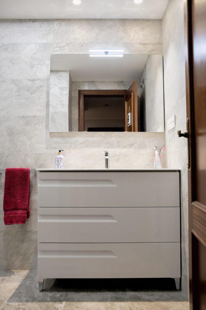 Reforma de baño mueble blanco con espacio de almacenamiento y espejo con luz incorporada