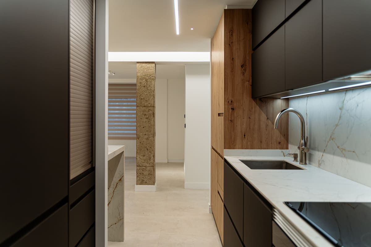 Vista lateral de una cocina moderna en gris mate y madera con encimera en porcelánico