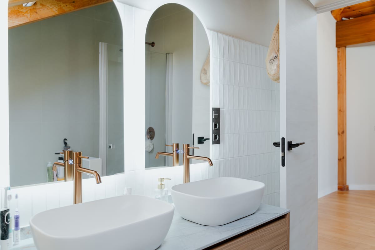 Baño con doble lavabo, grifería negra empotrada y revestimientos porcelánicos claros.