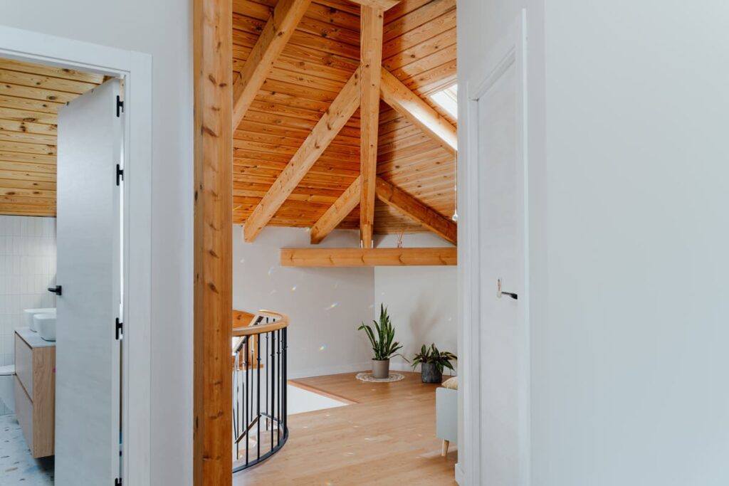Distribuidor bajo cubierta con estructura de madera vista, ventanas y nuevas puertas interiores.
