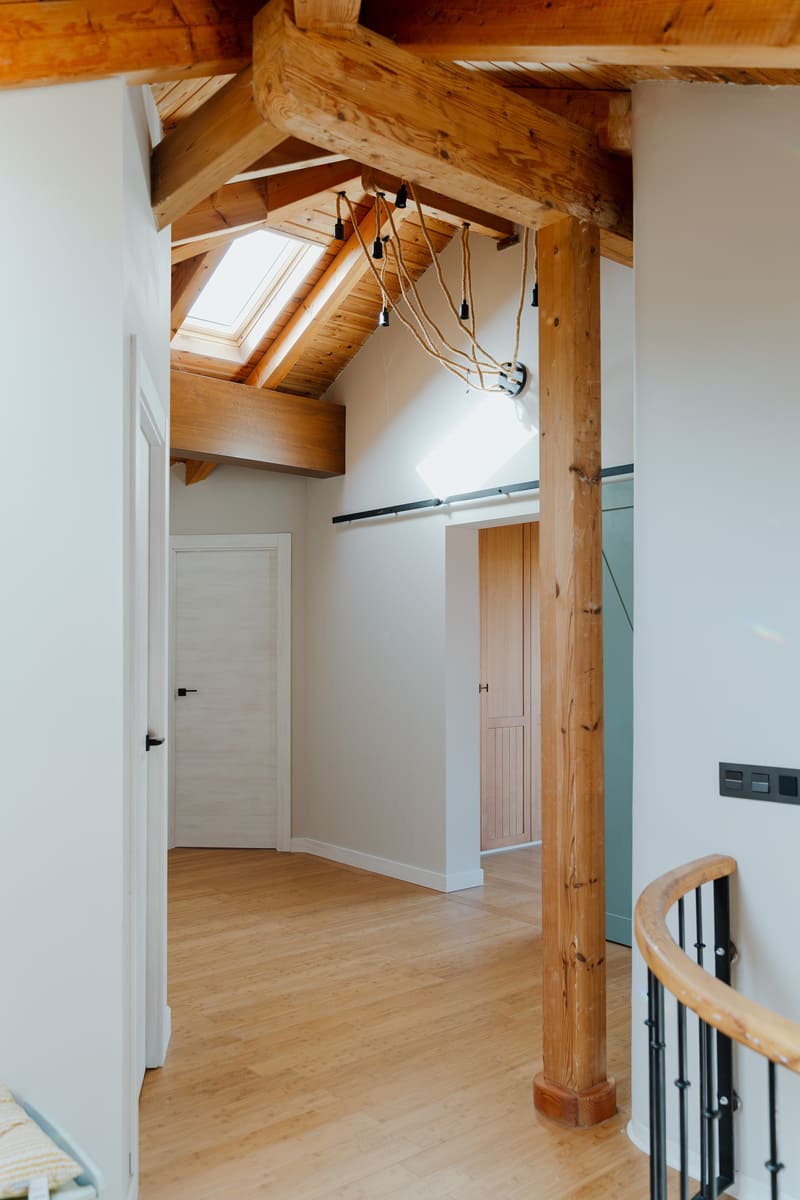 Distribuidor bajo cubierta con estructura de madera vista, ventanas y nuevas puertas interiores.