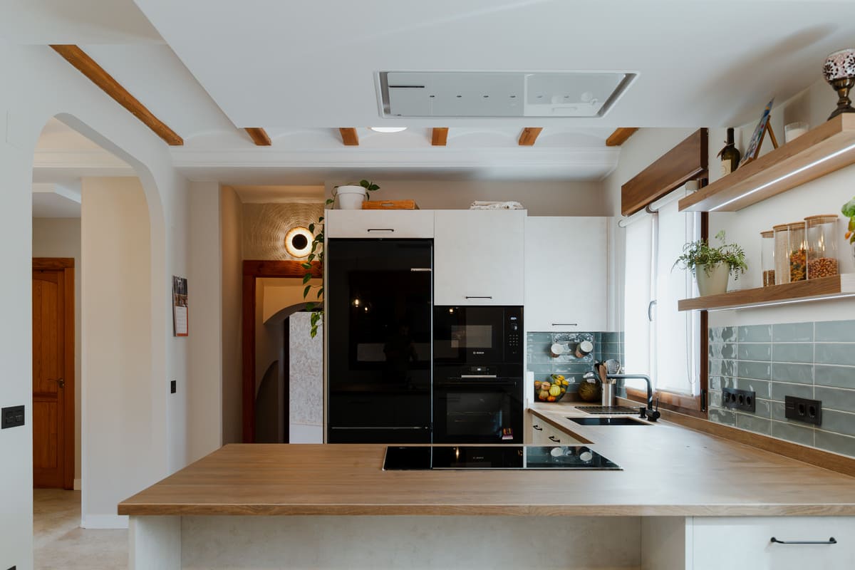 Cocina abierta con muebles verdes, madera y electrodomésticos negros en una reforma integral en Robledo de Torío.