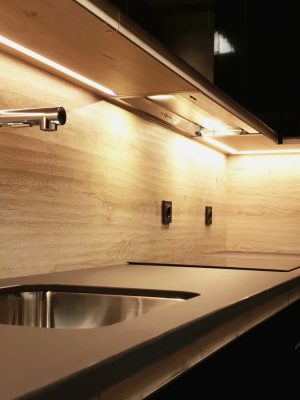 Detalle de encimera de cocina negra y madera en forma de "L" con fregadero integrado, placa de inducción con una campana incorporada y leds