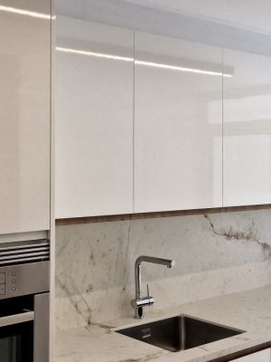 Frente de cocina moderna blanca con muebles altos, bajos y columna con horno, en color blanco brillo y tirador uñero en melamina roble dorado